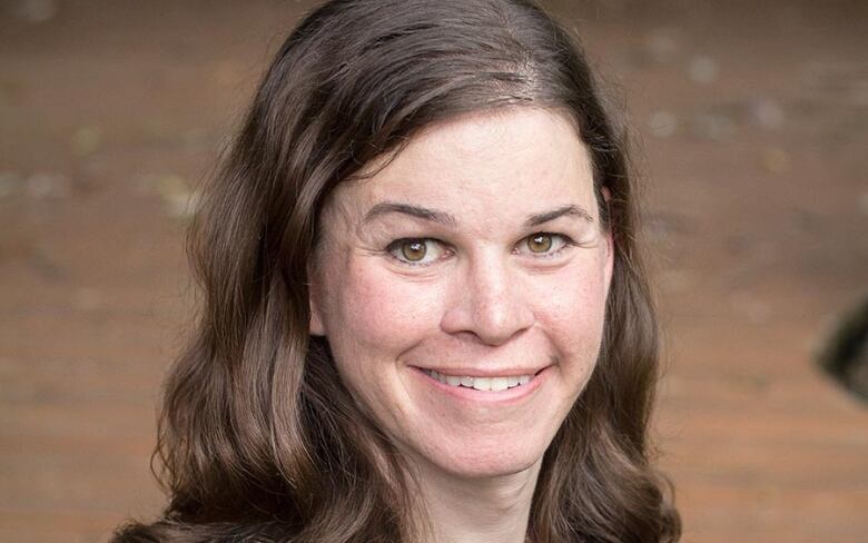 A headshot of a smiling woman with long, light brown hair.