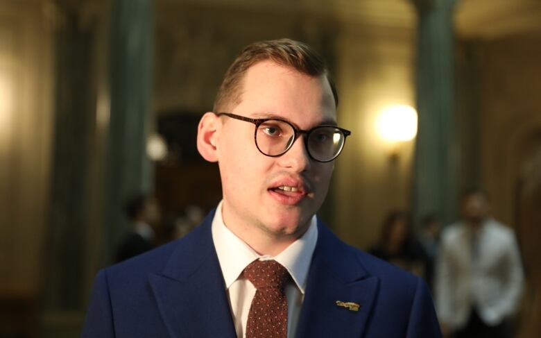 A man in a blue suit, white and red tie speaks with media. 