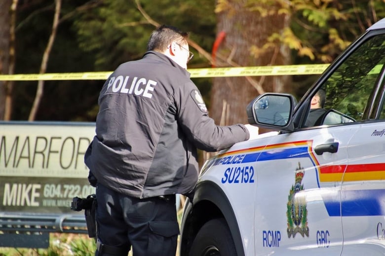 A man with a 'Police' jacket takes notes on the hood of a police car.