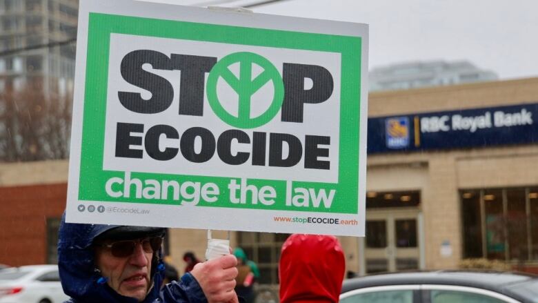 A protestor holding a sign that says 'stop ecocide, change the law'