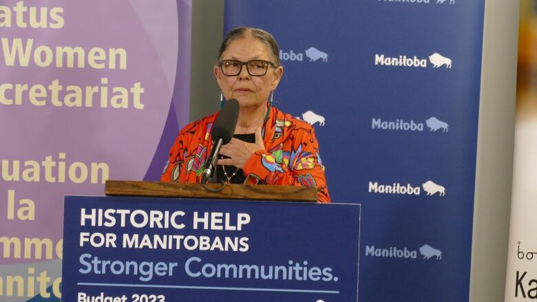 A woman standing at a podium, holding he left hand over her heart.