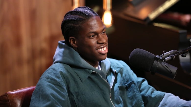 Singer-songwriter Daniel Caesar sits in front of a microphone smiling.