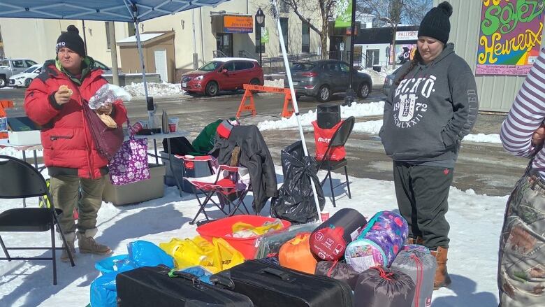 People standing outside near a table with some clothing on it.