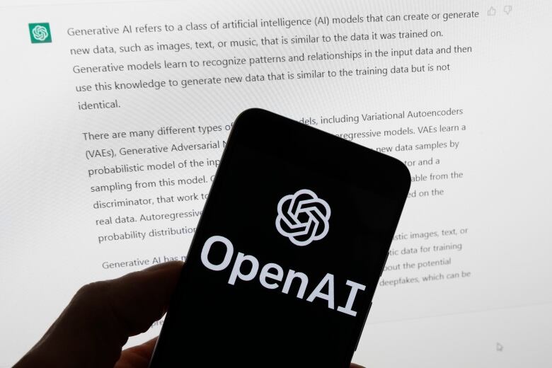 The OpenAI logo is seen on a mobile phone in front of a computer screen displaying output from ChatGPT, on March 21, 2023.