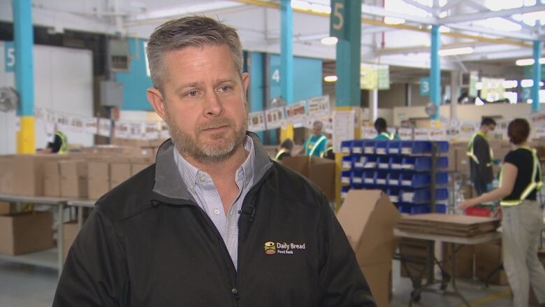 A man stands in a black jacket in a food bank.