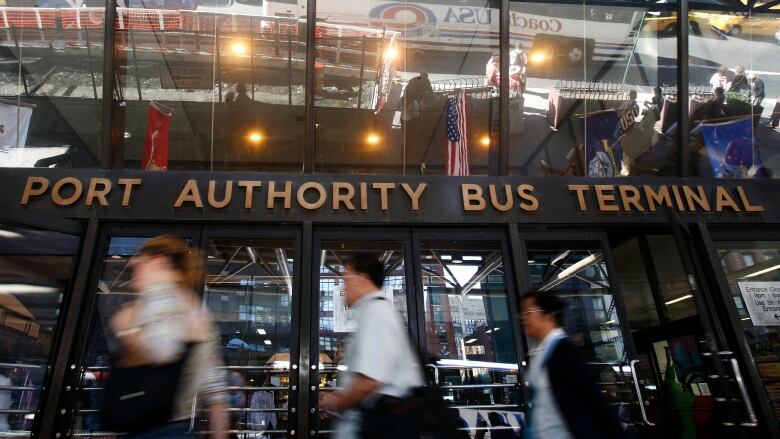 Entrance of the Port Authority Bus Terminal. Blurry people walking by the letter sign saying: Port Authority Bus Terminal