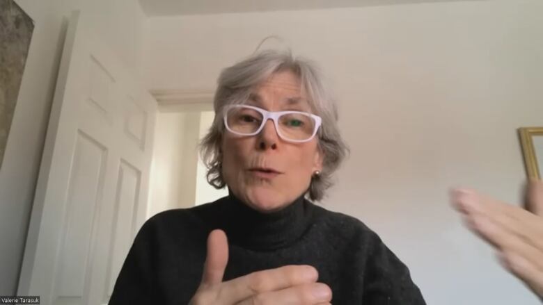 A women in a black turtleneck and white glasses on Zoom.