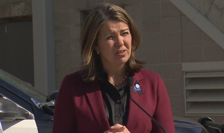 Smith wears a burgundy jacket with a blue pin as she squints in the sunlight speaking to reporters. 