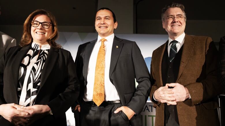 A woman and two men stand together and pose for a photo. 