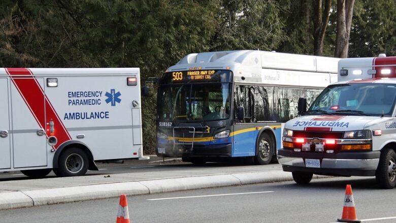 Two ambulances sit in front of a parked bus on a highway.