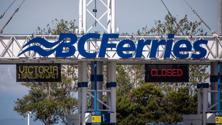 A sign reading 'B.C. Ferries' atop a parking booth, with two signs below it indicating certain lanes are open and closed.