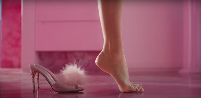 A woman's feet are shown as she stands on her toes next to a pair of pink shoes.