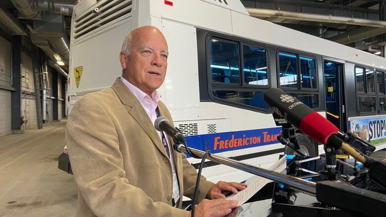 A man speaks while standing at a podium with a transit bus in the background.