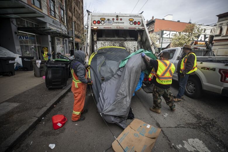 City workers throw a tent into a trash truck.