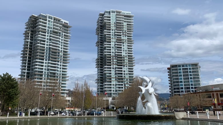 Three condo buildings with a pond and a dolphin-shaped statue in front of it.