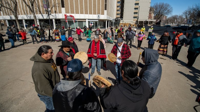 Drummers stand in a circle on a street, with other protesters in a circle around them.