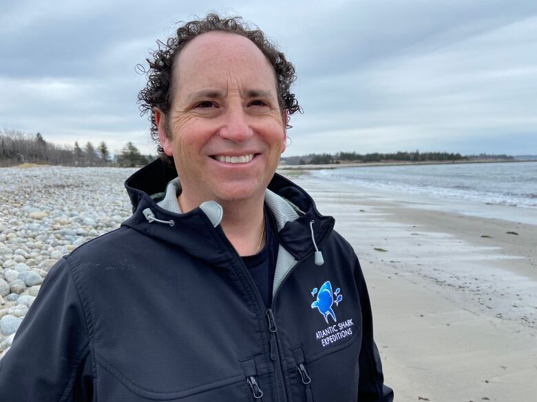 A man in a jacket emblazoned with Atlantic Shark Expeditions stands on a beach.