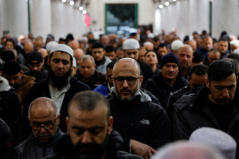 A group of people pray inside a mosque with their eyes closed.