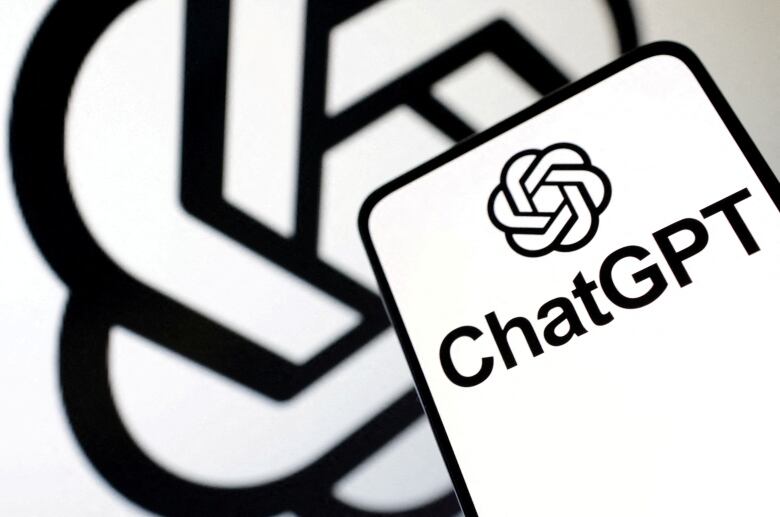 ChatGPT logo over a white background is pictured on a mobile phone held in front of a larger version of the logo.