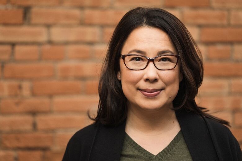 Smiling woman wearing a black cardigan and green t-shirt stands in front of a red brick wall.