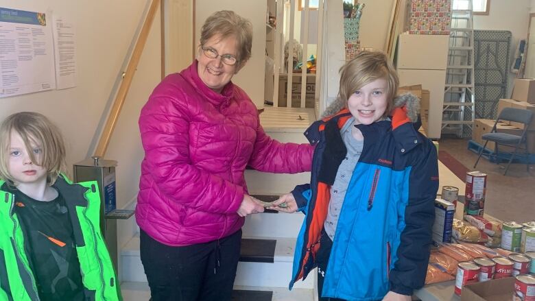 A woman poses between two young boys inside a house, as one of the young boys hands her something.