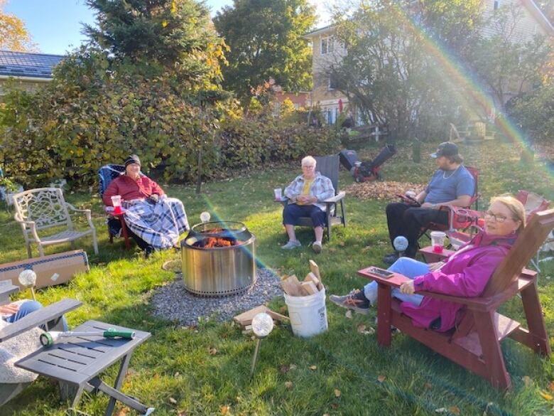 Four people sit around a backyard fire while the sun settles low.