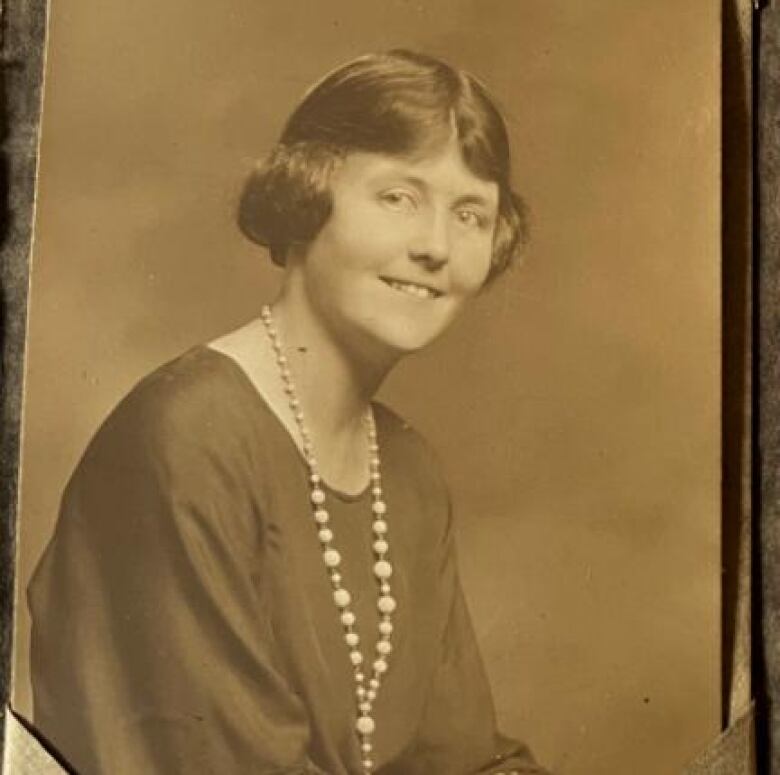 A woman in a dress with pearls around her neck.