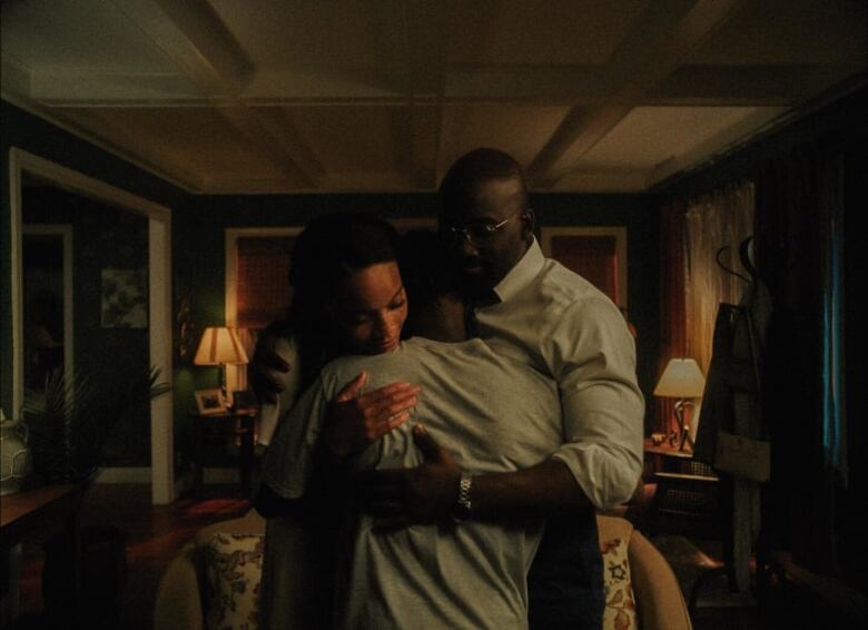 A man and a woman, facing the camera, hug a boy, facing away from the camera, in a living room. 