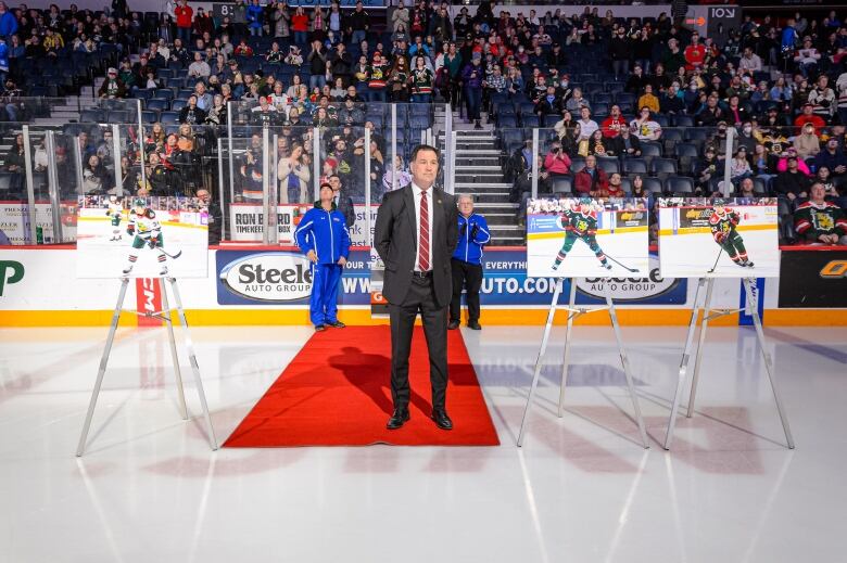 A man wearing a suit stands on a carpet at ice level.