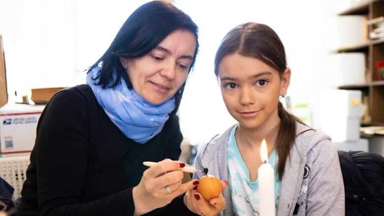 A woman and young girl decorate a Ukrainian Easter egg.