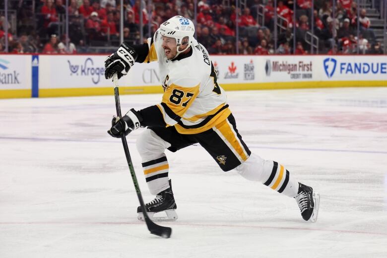 A male hockey player wearing a white, yellow and black Pittsburgh Penguins jersey reacts as he puts on a shot.