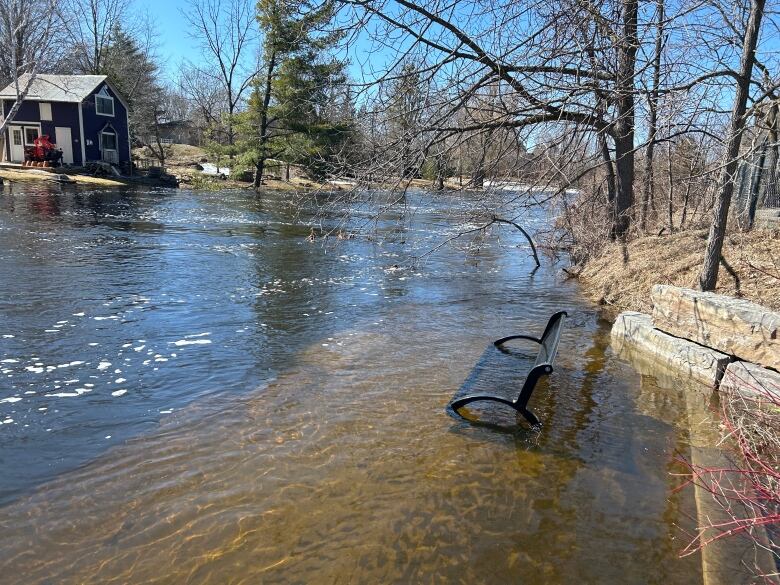 A bench is almost fully submerged underwater along the banks of a river. 