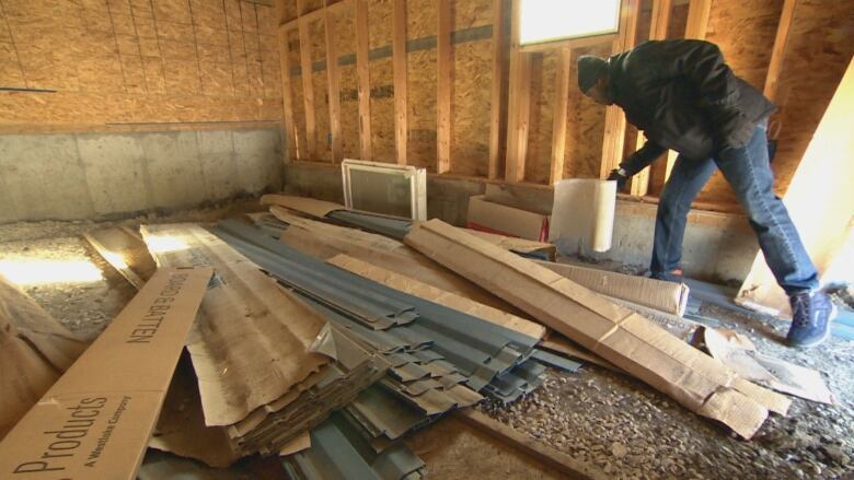 A man, surrounded by building materials, bends over.