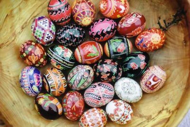 A wooden bowl is full of colourful decorated eggs