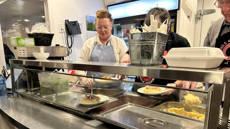 A woman scoops food onto a plate. 