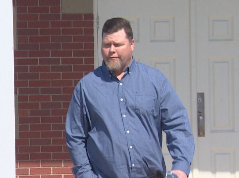 A man walking in front of a brick building with white front doors.