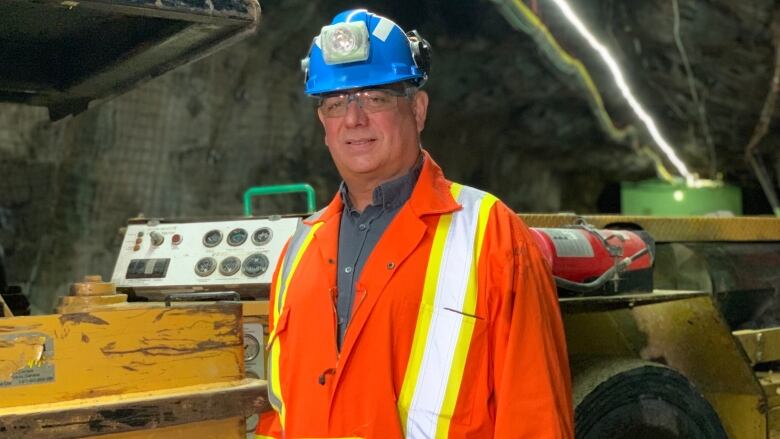 A man standing in an underground mine wearing orange coveralls and a blue hard hat.