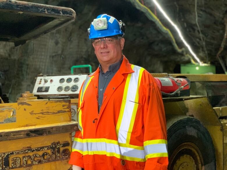 A man standing in an underground mine wearing orange coveralls and a blue hard hat.