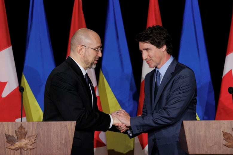 While smiling warmly, a man clasps the hands of another man at a podium in a Toronto hotel.