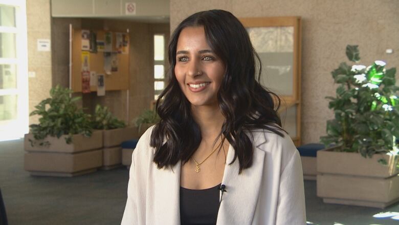 A medium-shot of a woman wearing a white lab coat. She has dark hair, is smiling and looking slightly off camera.  