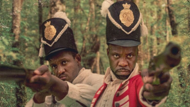 Two Black men wearing 19th century military uniforms point guns toward the viewer. They are in a forest. Both are scowling. 