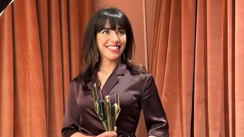 A lady in a purple dress holds a trophy.