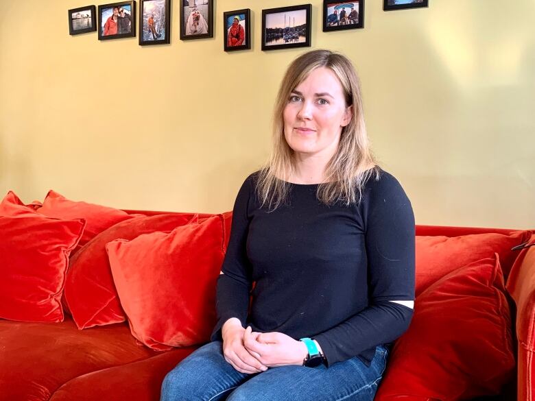 A woman with light brown hair and a long-sleeved black blouse sits on a red couch.