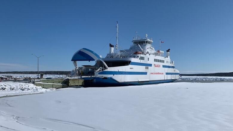 A big white boat beside a dock in a snowy ocean.