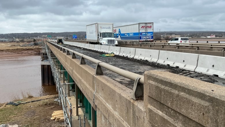 Two large trucks cross centre lane of bridge with left lane closed.