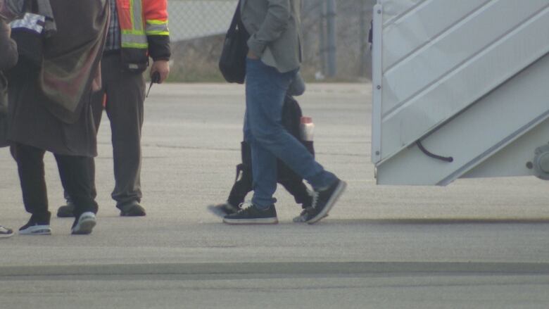 People are shown walking off a staircase from an airplane.