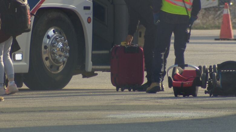 A red suitcase sitting next to a coach bus is picked up. 