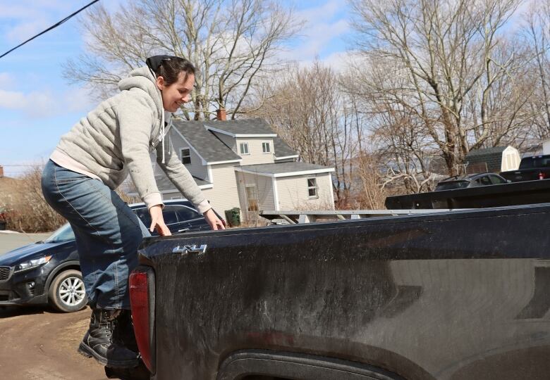 A woman hold on to the back of a parked black pickup truck.