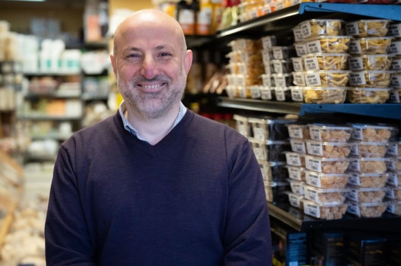 A man in a purple sweater is smiling in a grocery store.