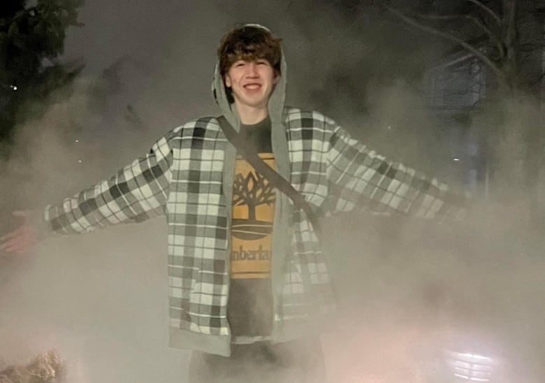 A teen boy stands in a cloud of mist or steam, smiling.